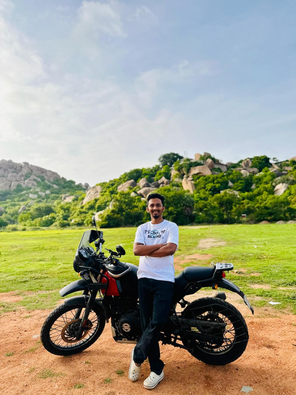 Me standing beside by bike against Hampi's green and rocky landscape